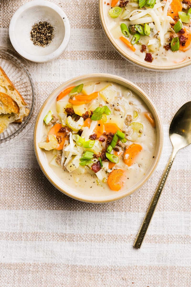 A bowl of creamy hamburger potato soup with crumbled bacon, green onions and cheese.