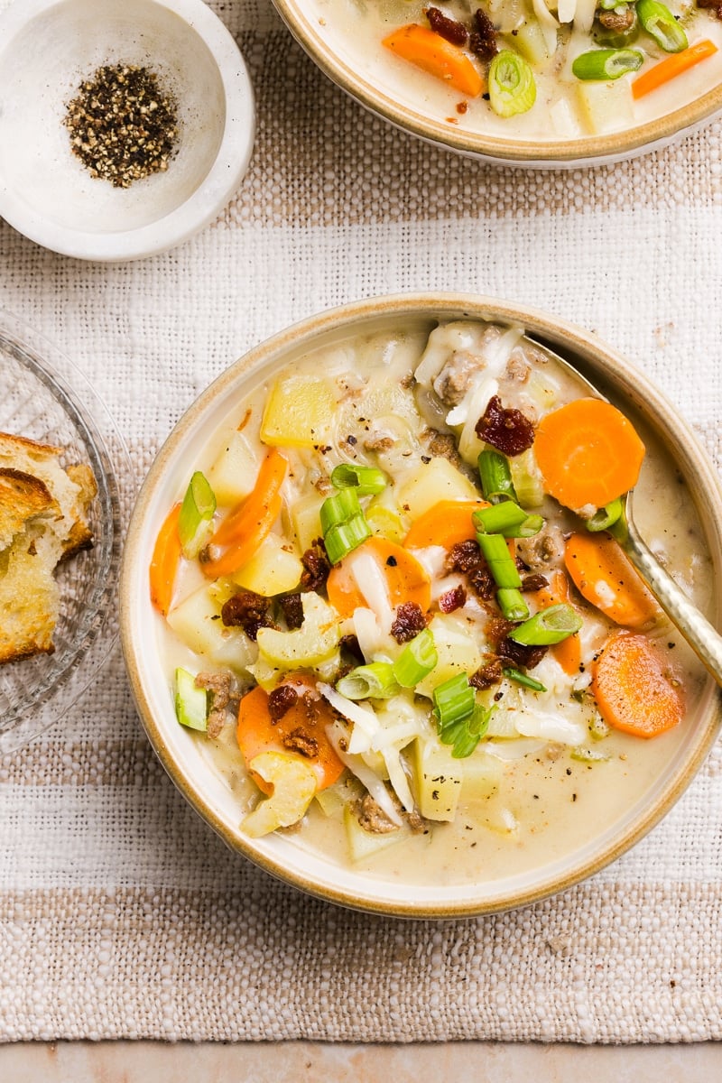 A bowl of creamy hamburger potato soup with crumbled bacon, green onions and cheese.