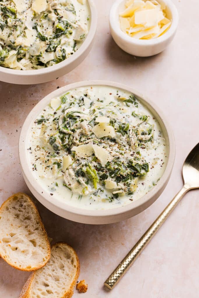 Chicken spinach artichoke soup in a bowl topped with parmesan cheese.