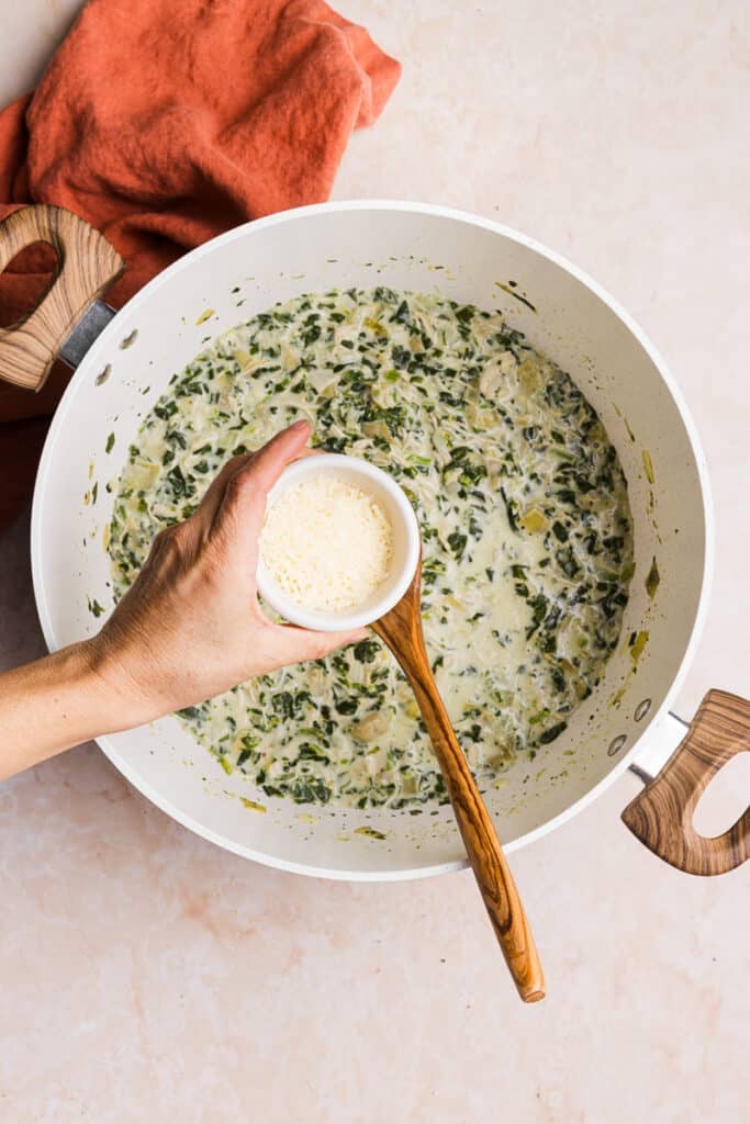 Parmesan cheese being added to chicken spinach artichoke soup.