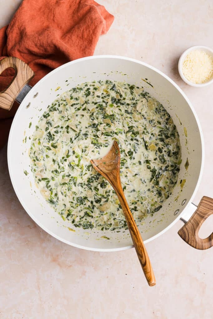 Chicken spinach artichoke soup in a pot with a wooden spoon.
