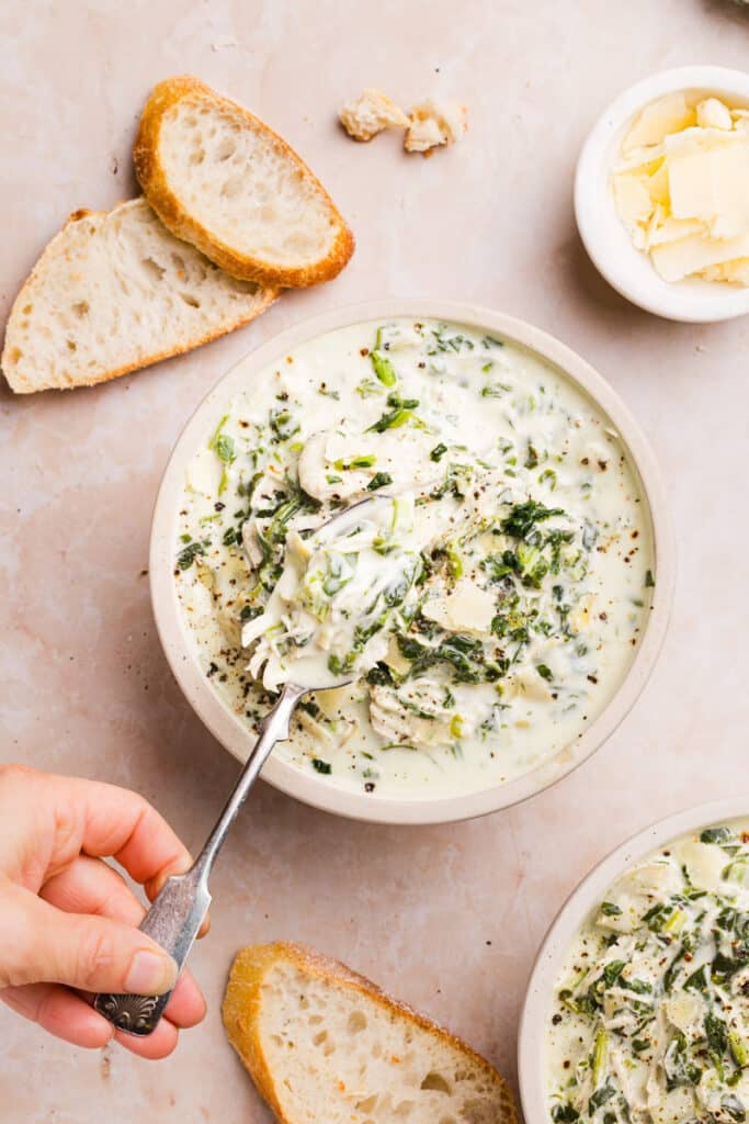 Chicken spinach artichoke soup in a bowl with a spoon.
