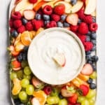 A platter of fruit with cottage cheese fruit dip in a bowl.