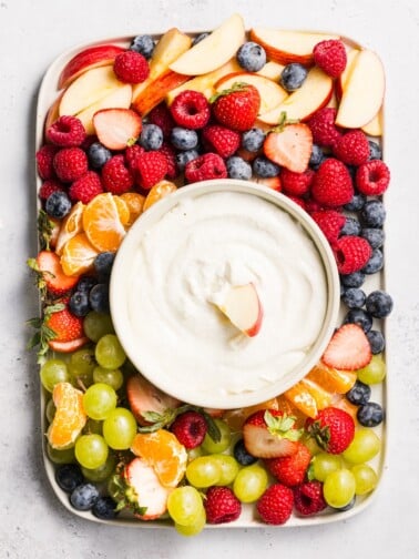 A platter of fruit with cottage cheese fruit dip in a bowl.