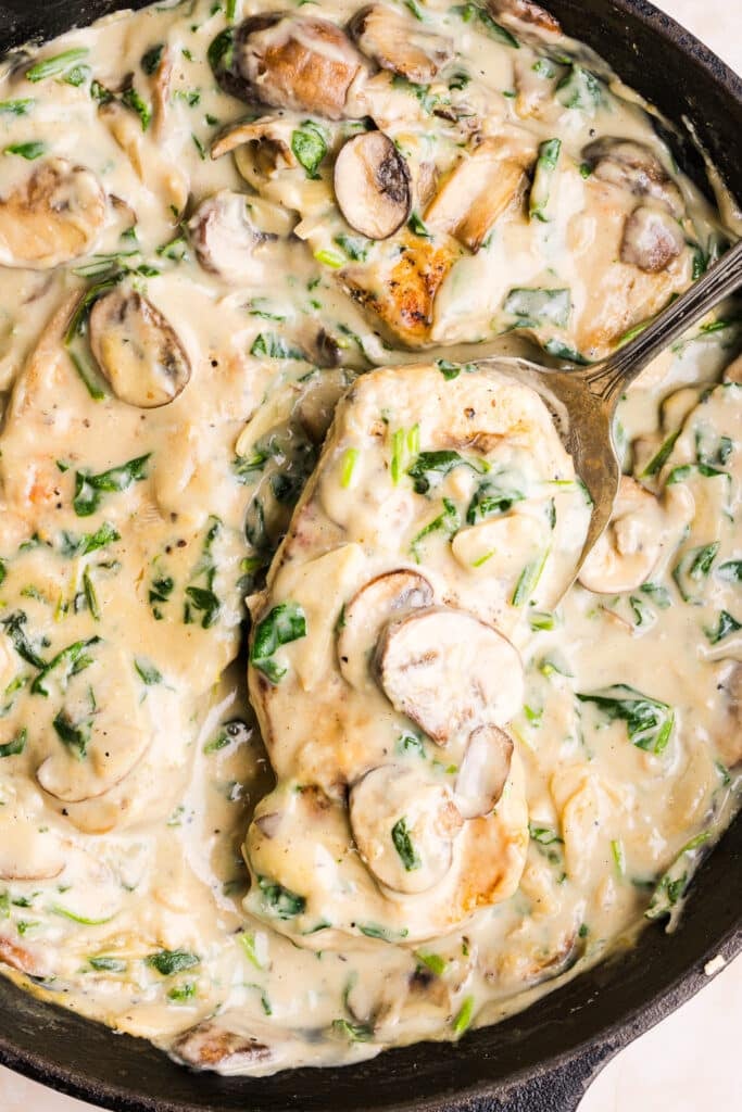 Creamy garlic pork chops in a pan with a large spoon.