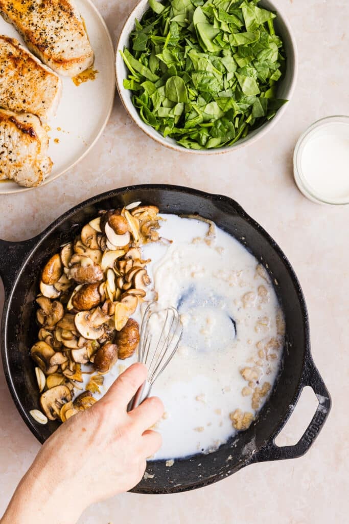 Milk being added to a pan with mushrooms to make a creamy sauce.