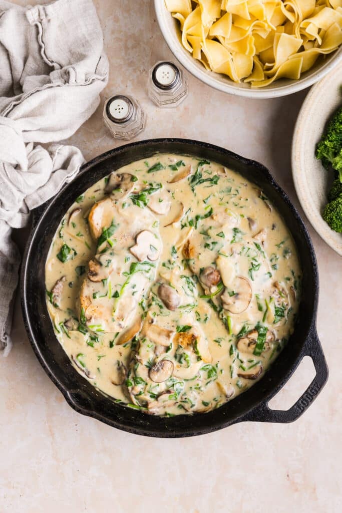Creamy garlic pork chops in a pan with spinach and mushrooms.