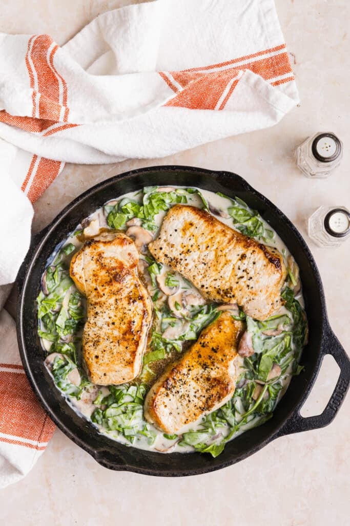 Pork chops being added back to a pan with veggies and a creamy garlic sauce.
