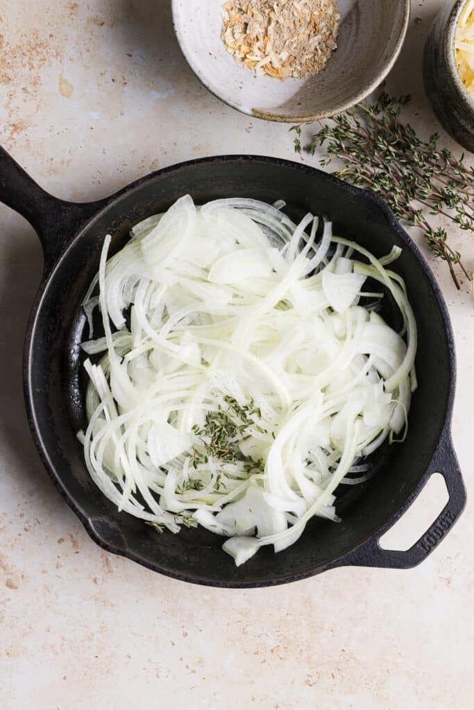 Thinly sliced onions and thyme in a frying pan.