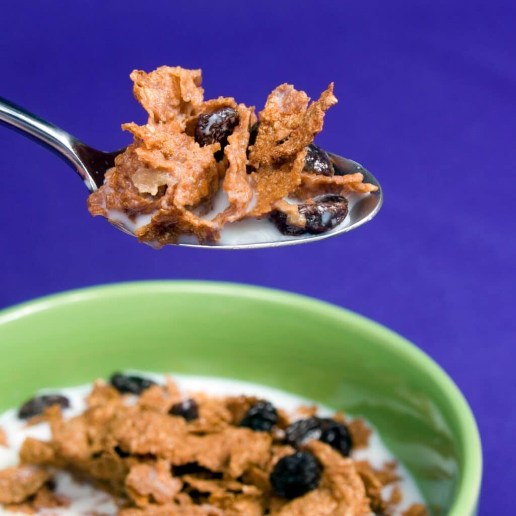 A spoonful of Raisin bran cereal from a green bowl with milk.