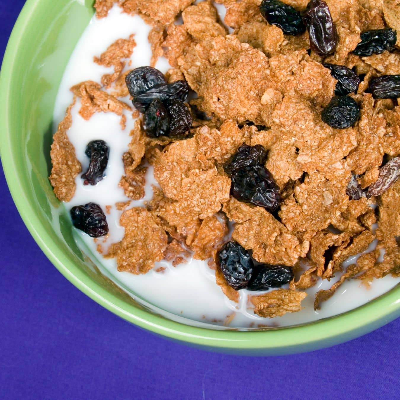 Raisin Bran with milk in a green bowl.