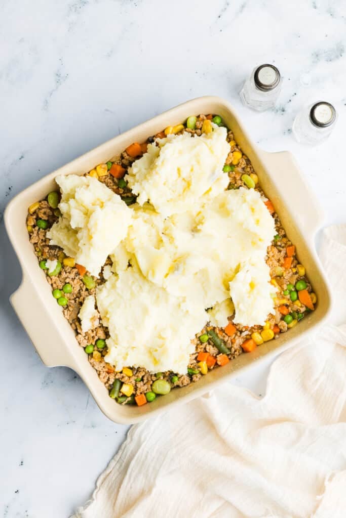 Mashed potatoes being added to the top of a ground turkey and veggie mixture.