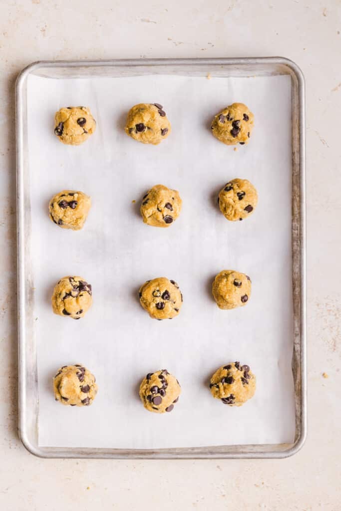 Whole wheat cookie dough scooped onto a baking sheet lined with parchment paper.