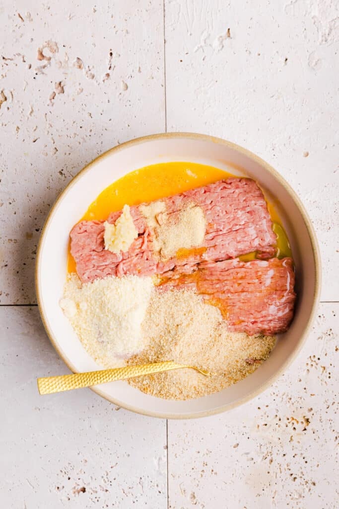 Ground turkey, breadcrumbs, egg, parmesan cheese and spices being mixed up in a bowl.