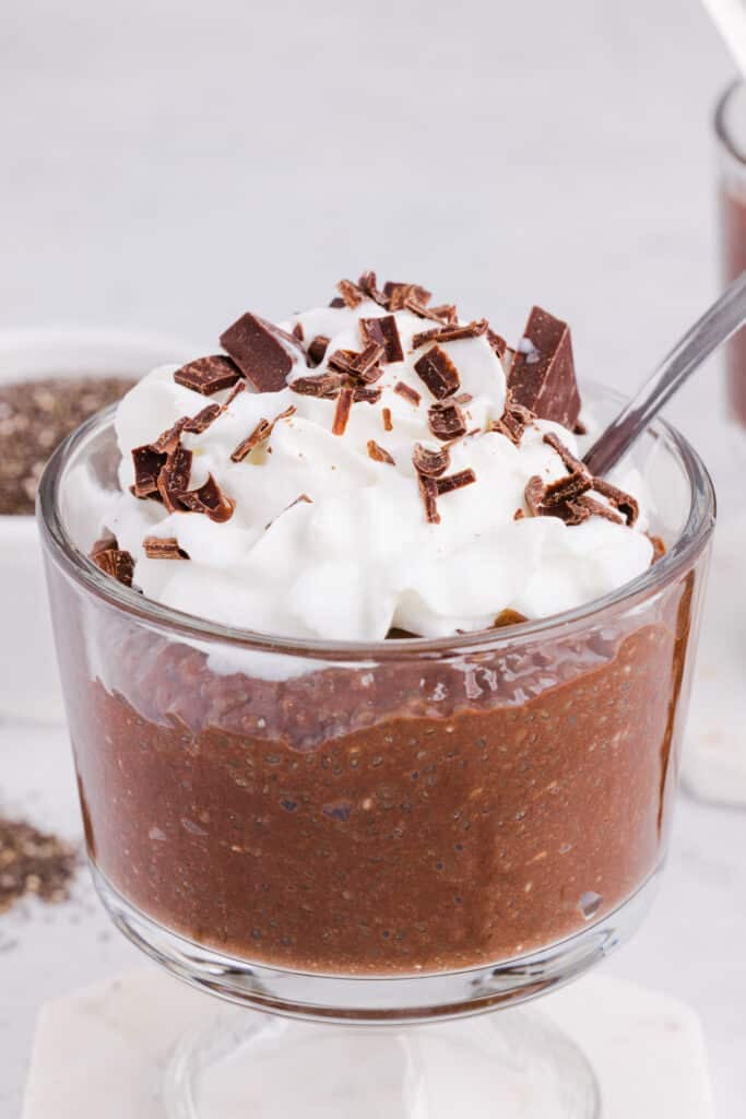 Chocolate blended chia seed pudding in a glass with whipped cream and chocolate shavings.