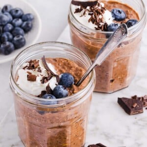 Chocolate protein overnight oats in jars with whipped cream, chocolate shavings and blueberries.