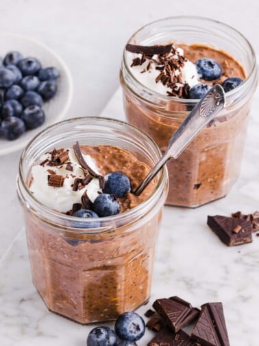 Chocolate protein overnight oats in jars with whipped cream, chocolate shavings and blueberries.