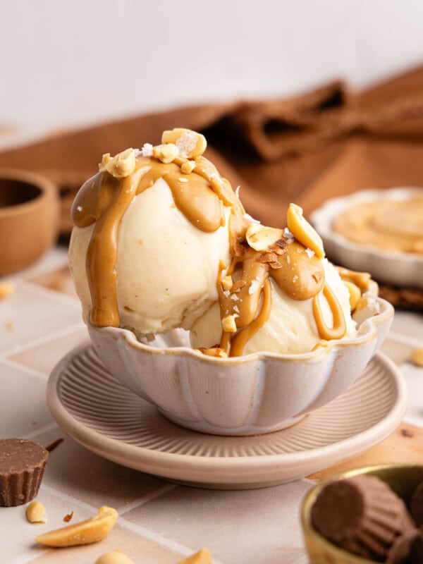 Two scoops of peanut butter ice cream made in the ninja creami sit in a bowl with peanut butter drizzle and crushed peanuts on top.