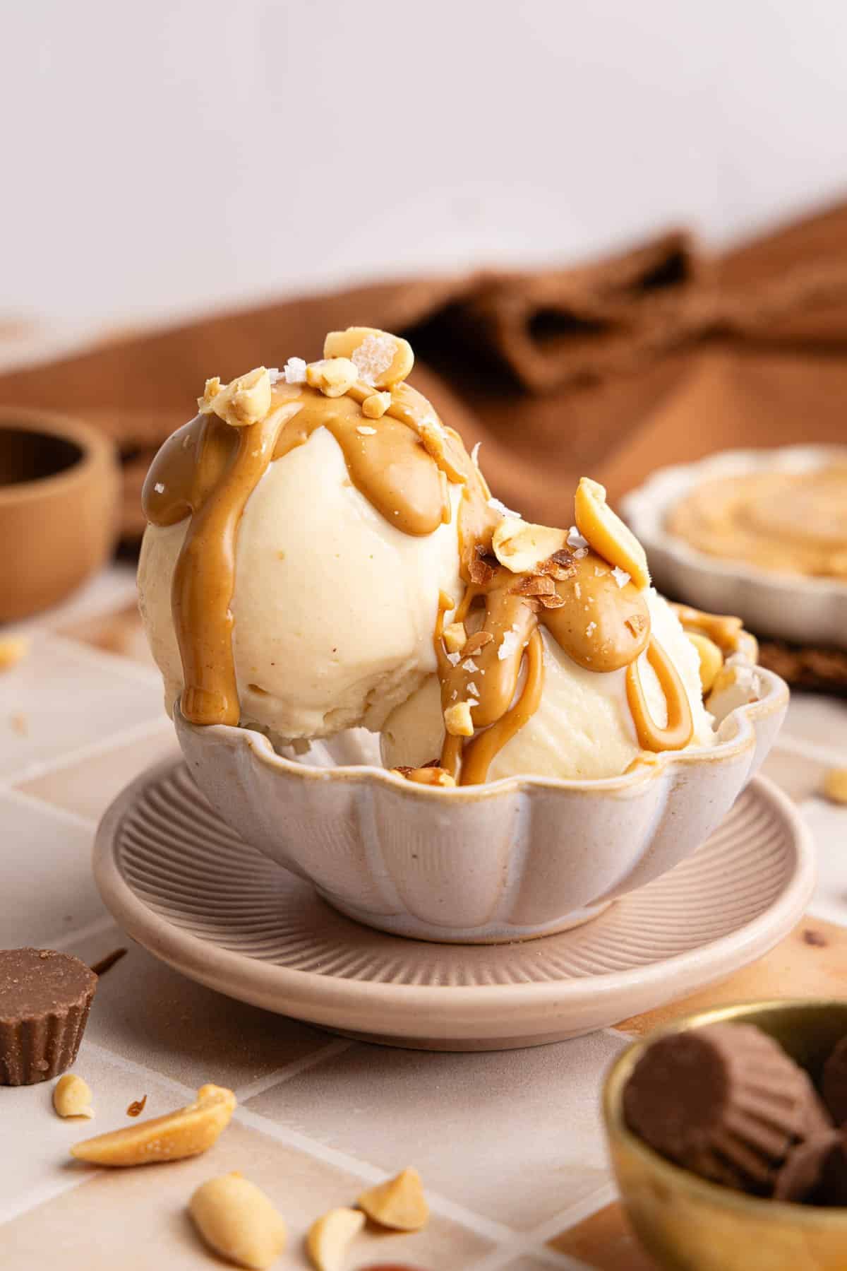 Two scoops of peanut butter ice cream made in the ninja creami sit in a bowl with peanut butter drizzle and crushed peanuts on top.