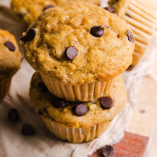 To kodiak cakes banana muffins stacked on a wooden board.