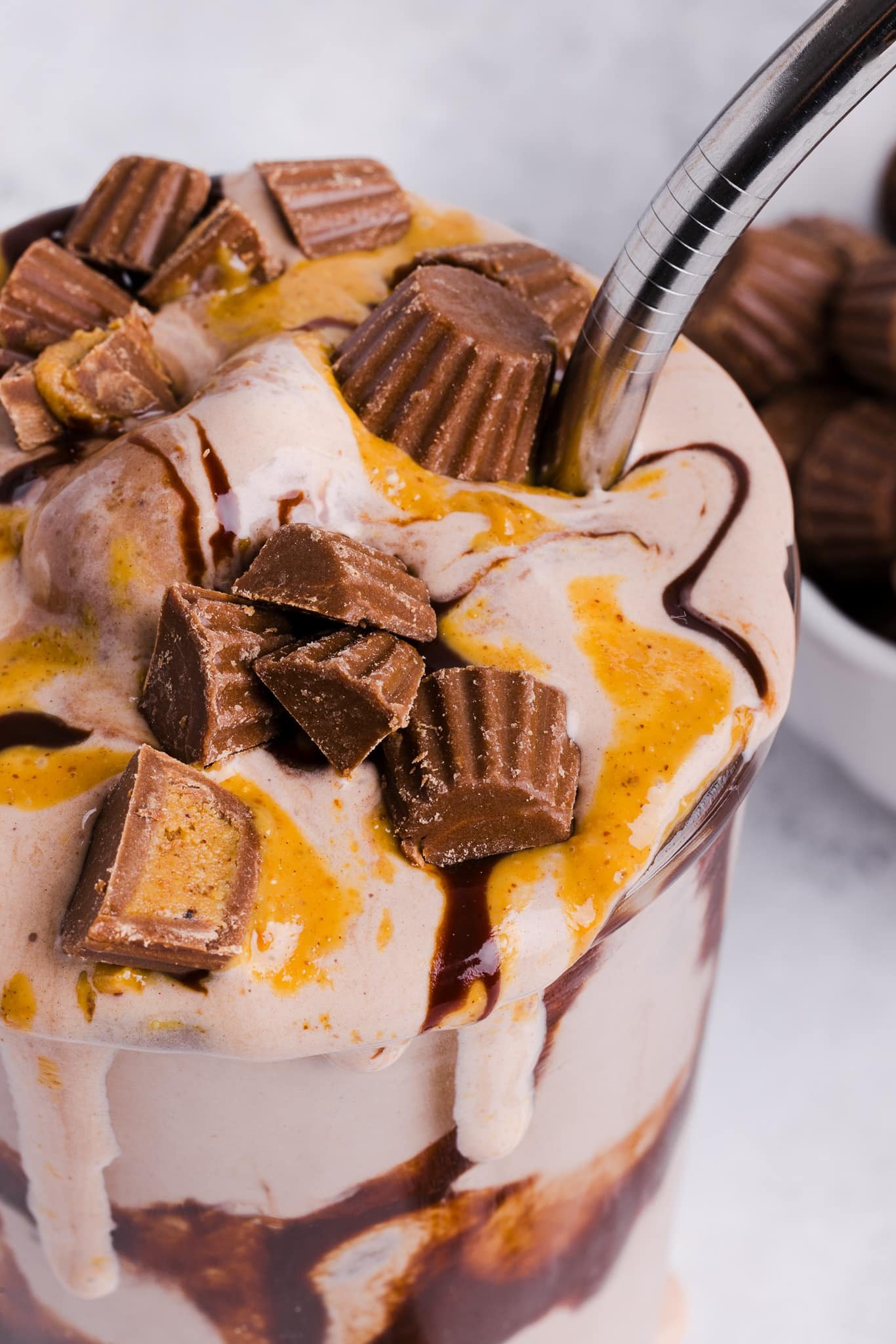 A close up shot of a Ninja Creami milkshake topped with peanut butter cups and drizzled with peanut butter and chocolate sauce.