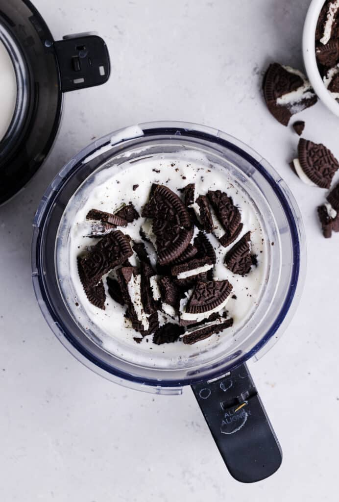 Oreos being added to the Ninja Creami pint container for a milkshake.