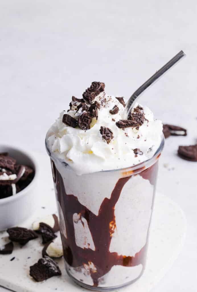 Ninja Creami Oreo Milkshake in a glass with whipped cream, crushed Oreos and chocolate sauce.