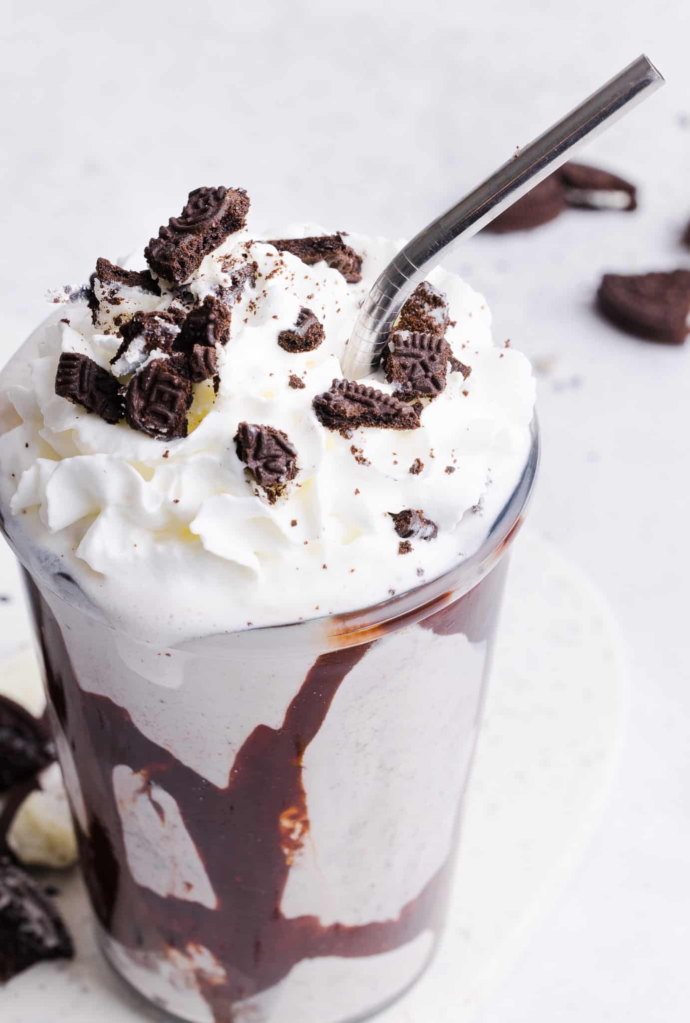Ninja Creami Oreo Milkshake in a glass with whipped cream, crushed Oreos and chocolate sauce.