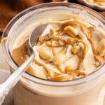 A spoon sits in a container of Ninja Creami Peanut Butter that was drizzled with peanut butter and chopped peanuts.