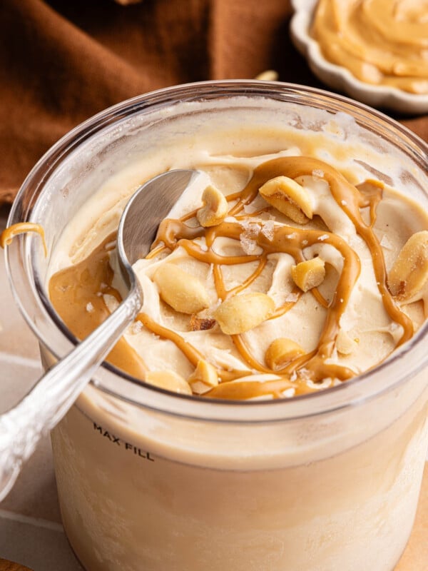 A spoon sits in a container of Ninja Creami Peanut Butter that was drizzled with peanut butter and chopped peanuts.