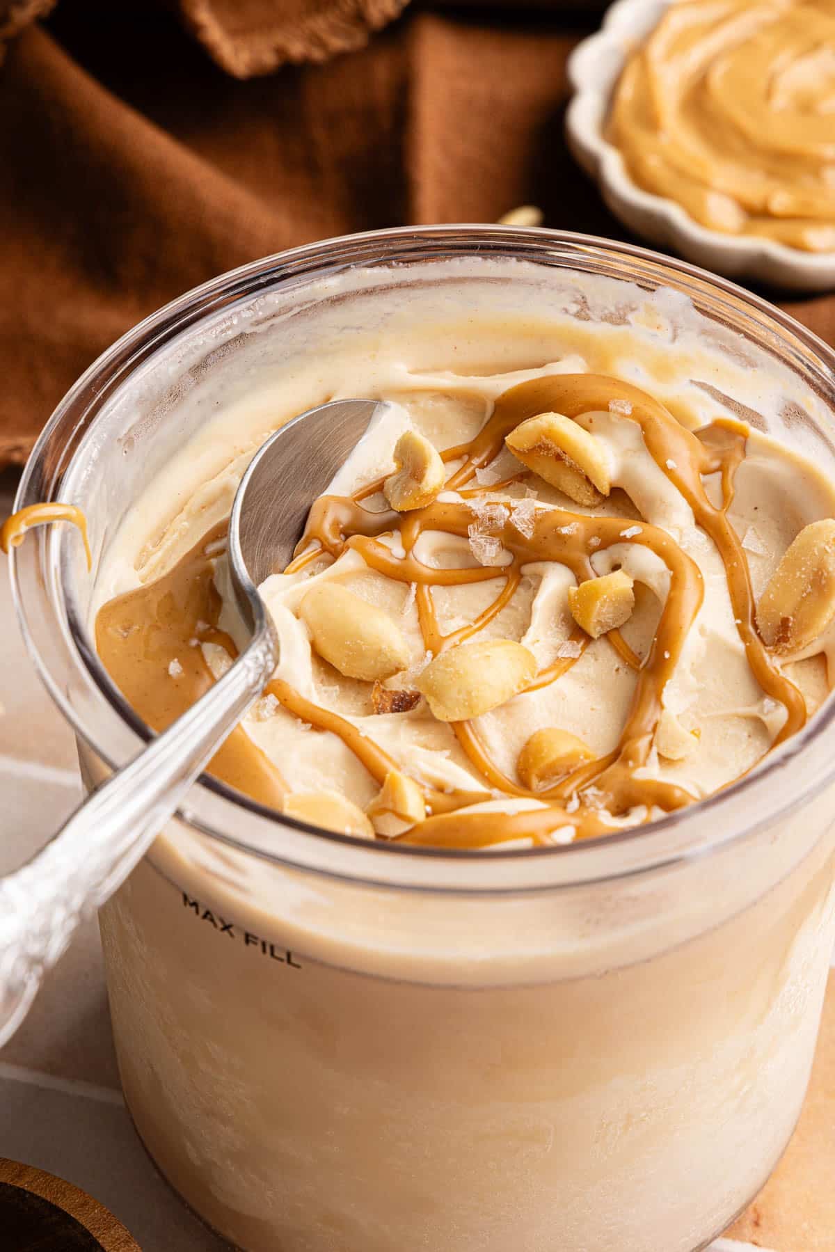 A spoon sits in a container of Ninja Creami Peanut Butter that was drizzled with peanut butter and chopped peanuts.