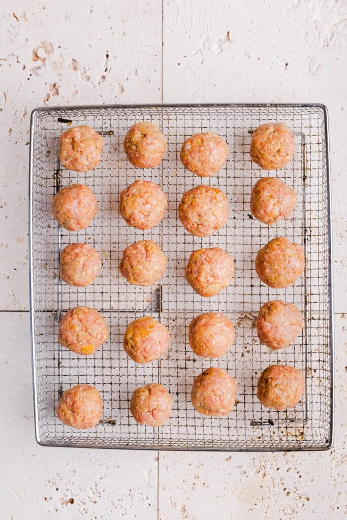 Raw turkey meatballs formed in an air fryer basket ready for the air fryer.