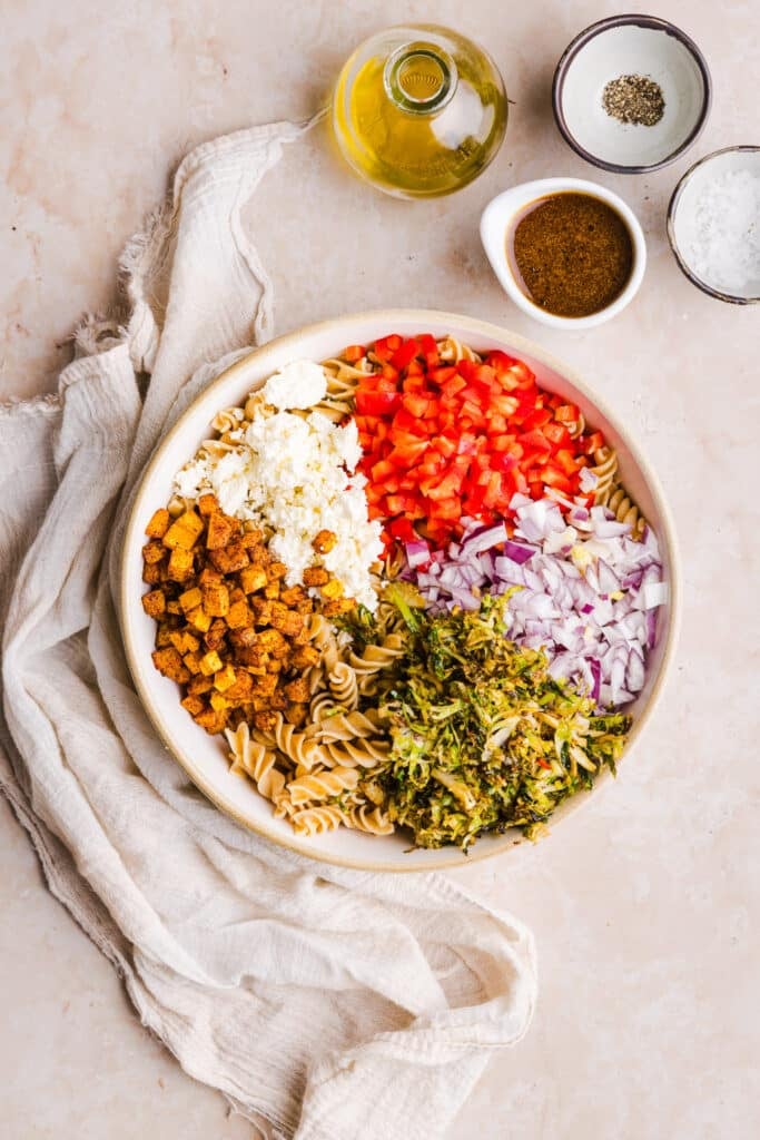 Winter pasta salad with whole wheat pasta, brussels sprouts, feta cheese, peppers, butternut squash and onions in a bowl.
