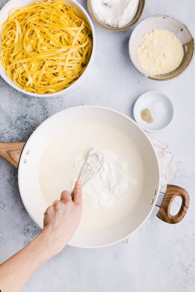 Greek yogurt Alfredo sauce being whisked together in a pan.