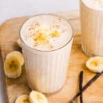 Two banana date smoothies on a cutting board with sliced bananas, vanilla beans and dates.