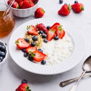 Cottage cheese, blueberries, strawberries and granola in a white bowl with a drizzle of honey.