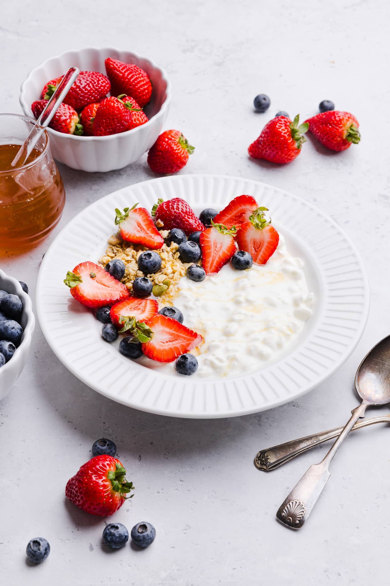 Cottage cheese, blueberries, strawberries and granola in a white bowl with a drizzle of honey.