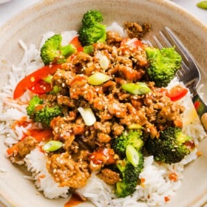 Firecracker ground chicken in a bowl with rice and broccoli, topped with sriracha.