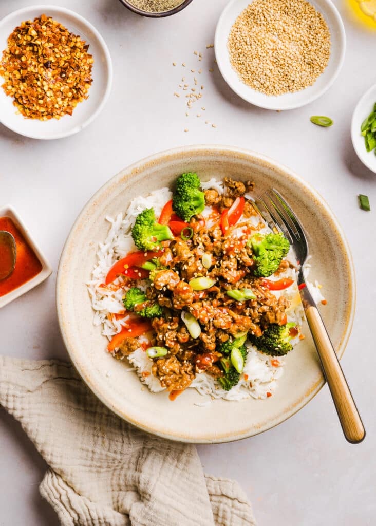 Firecracker ground chicken in a bowl with rice and broccoli, topped with sriracha.