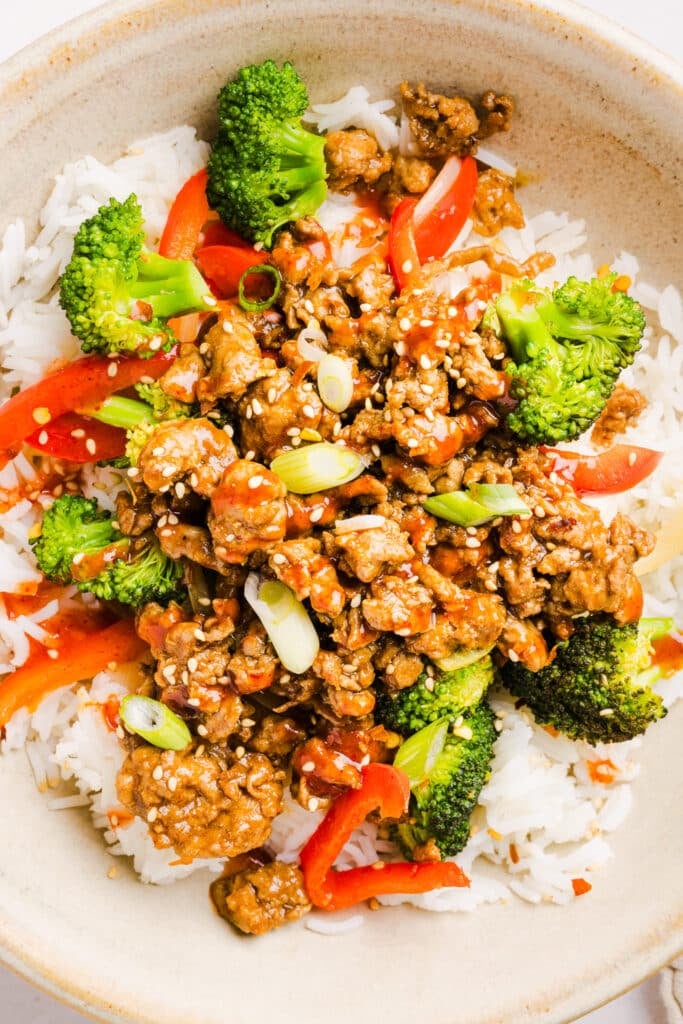 Firecracker ground chicken in a bowl with rice and broccoli, topped with sriracha.