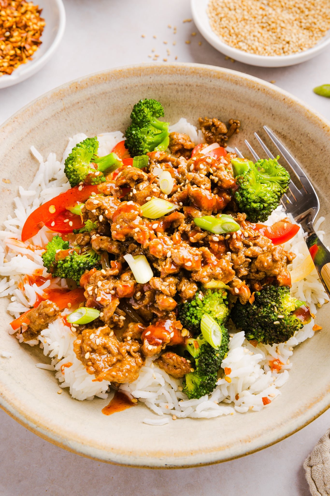 Firecracker ground chicken in a bowl with rice and broccoli, topped with sriracha.