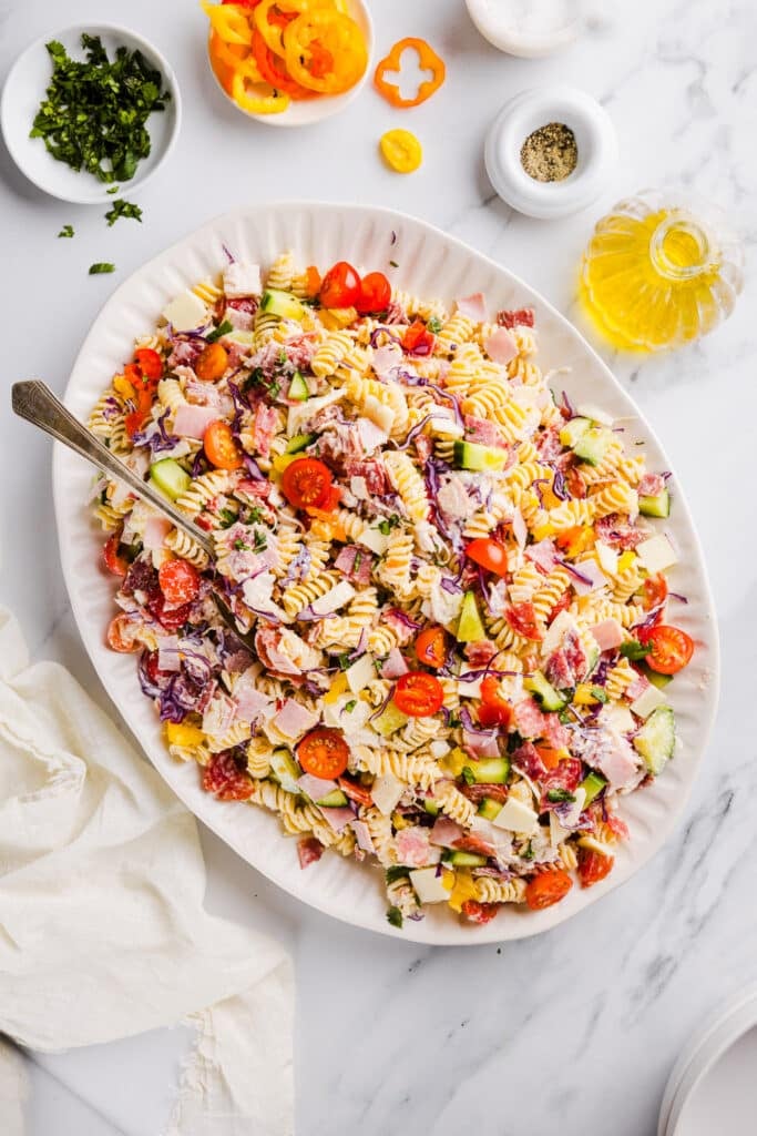 Grinder pasta salad on a large white platter with a serving spoons.