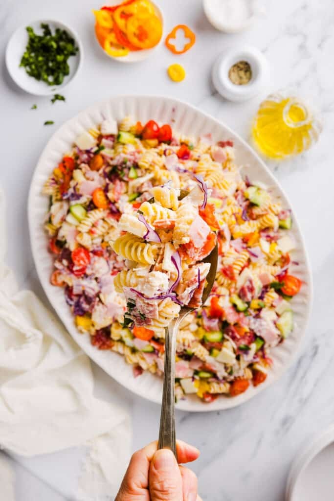 A spoonful of grinder pasta salad with a platter full of grinder pasta salad in the background.