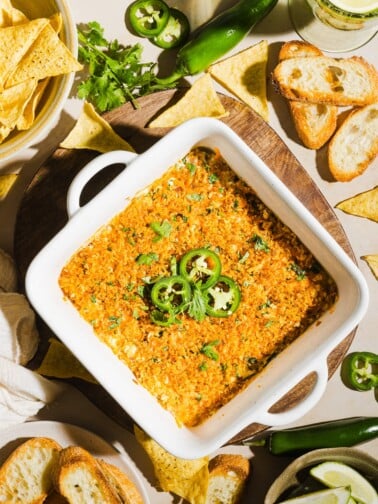 High protein jalapeño popper dip in a white ceramic baking dish, garnished with jalapeños and served with crostini.