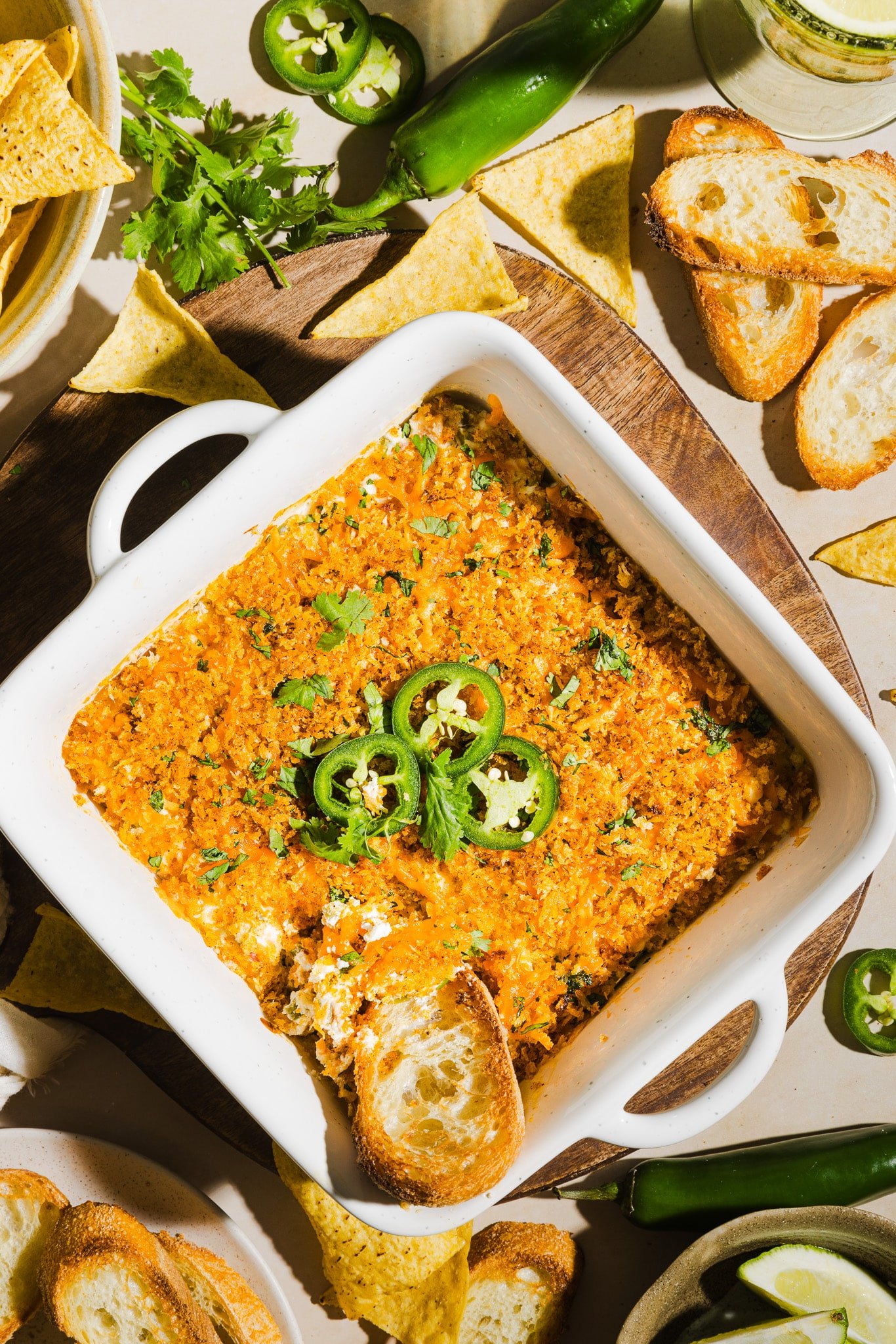 High protein jalapeño popper dip in a white ceramic baking dish, garnished with jalapeños and served with crostini.