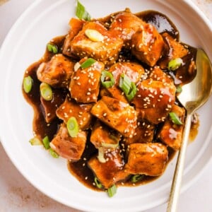 Teriyaki salmon bites in a serving dish garnished with green onion and sesame seeds.