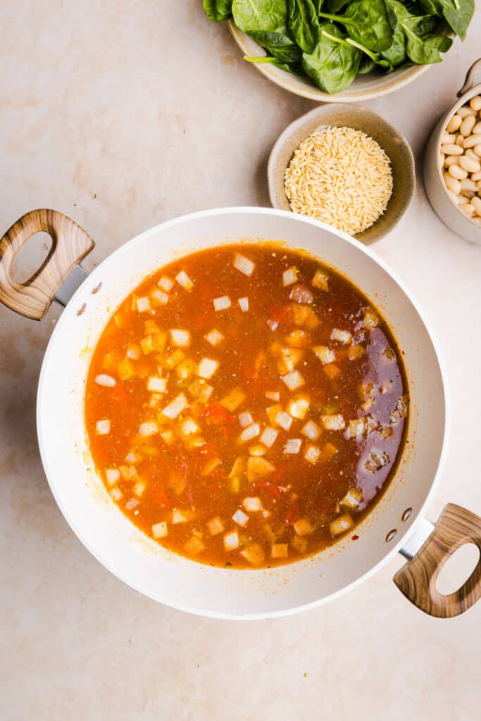 Vegetable orzo soup being cooked in a large pot.