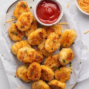 Cheese chicken nuggets on a platter with parchment paper and ketchup.