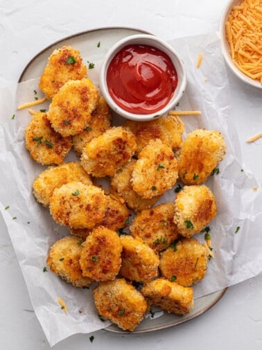 Cheese chicken nuggets on a platter with parchment paper and ketchup.
