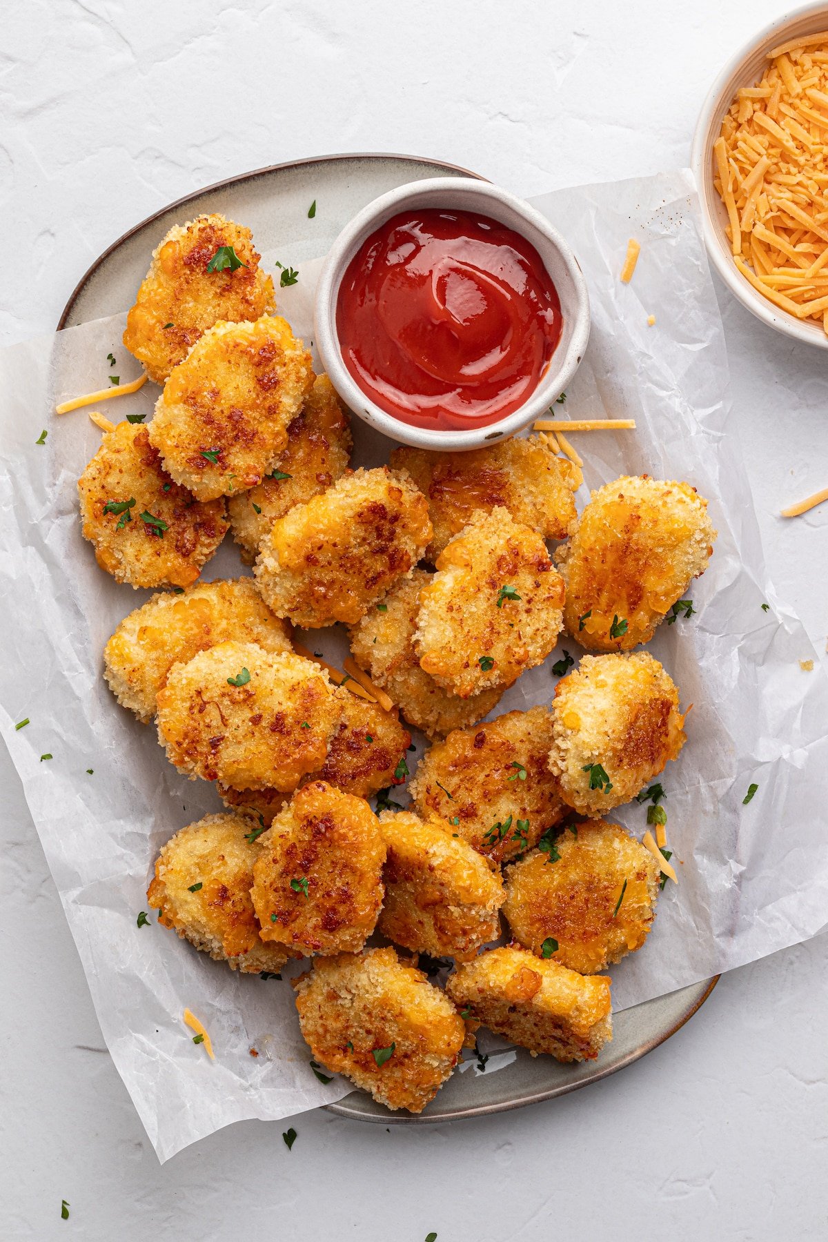 Cheese chicken nuggets on a platter with parchment paper and ketchup.